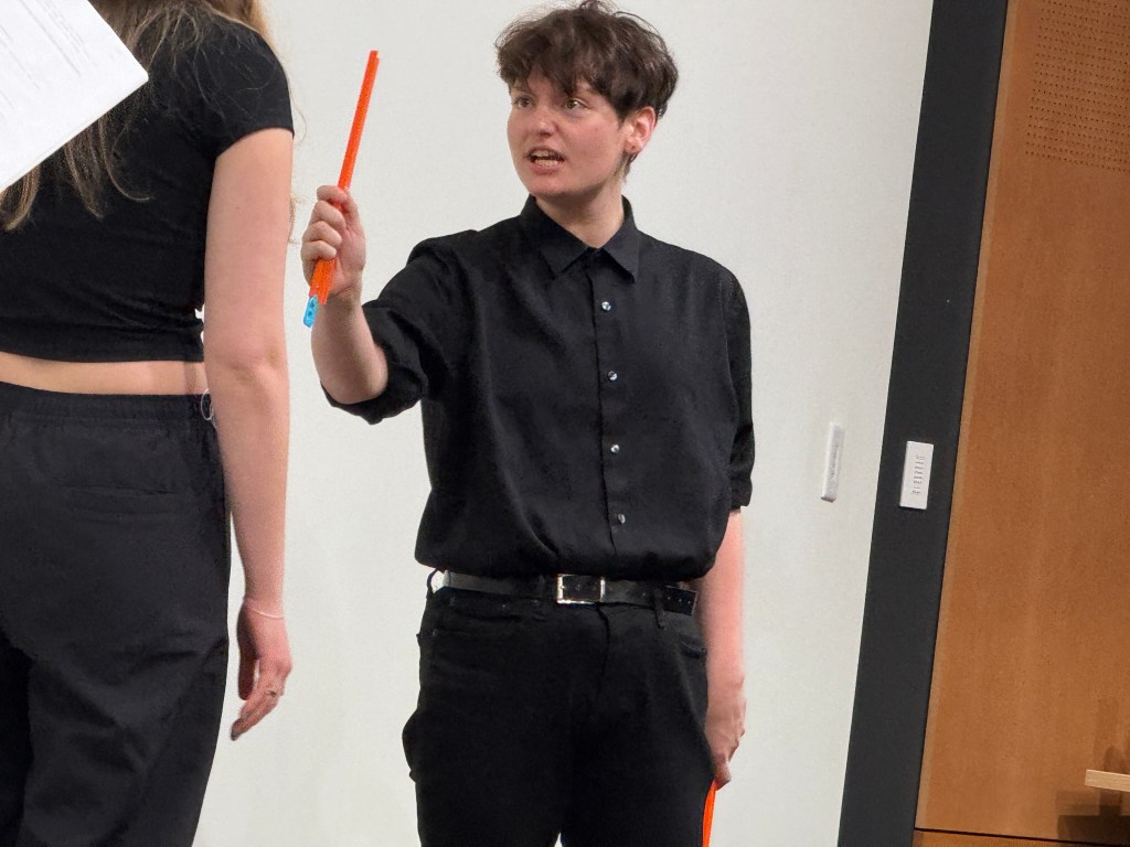 Tobias Sanders holding a piece of hot wheels track angrily in in "Apathy" in the Facility for Rare Isotope Beam (FRIB) Produced by Second Stage Playwriting