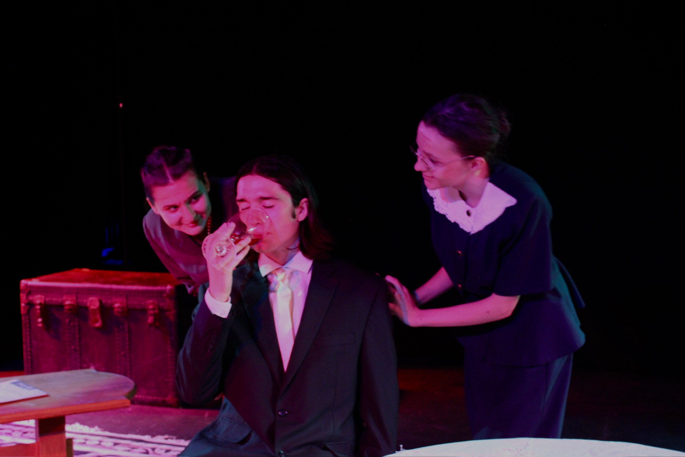 Iris Widlansky as Abby Brewster and Caitlyn Myers as Jonathan Brewster watching Sorine Andronic as Mr. Witherspoon drink poisoned wine in Second Stage Productions "Arsenic and Old Lace" under purple lighting
