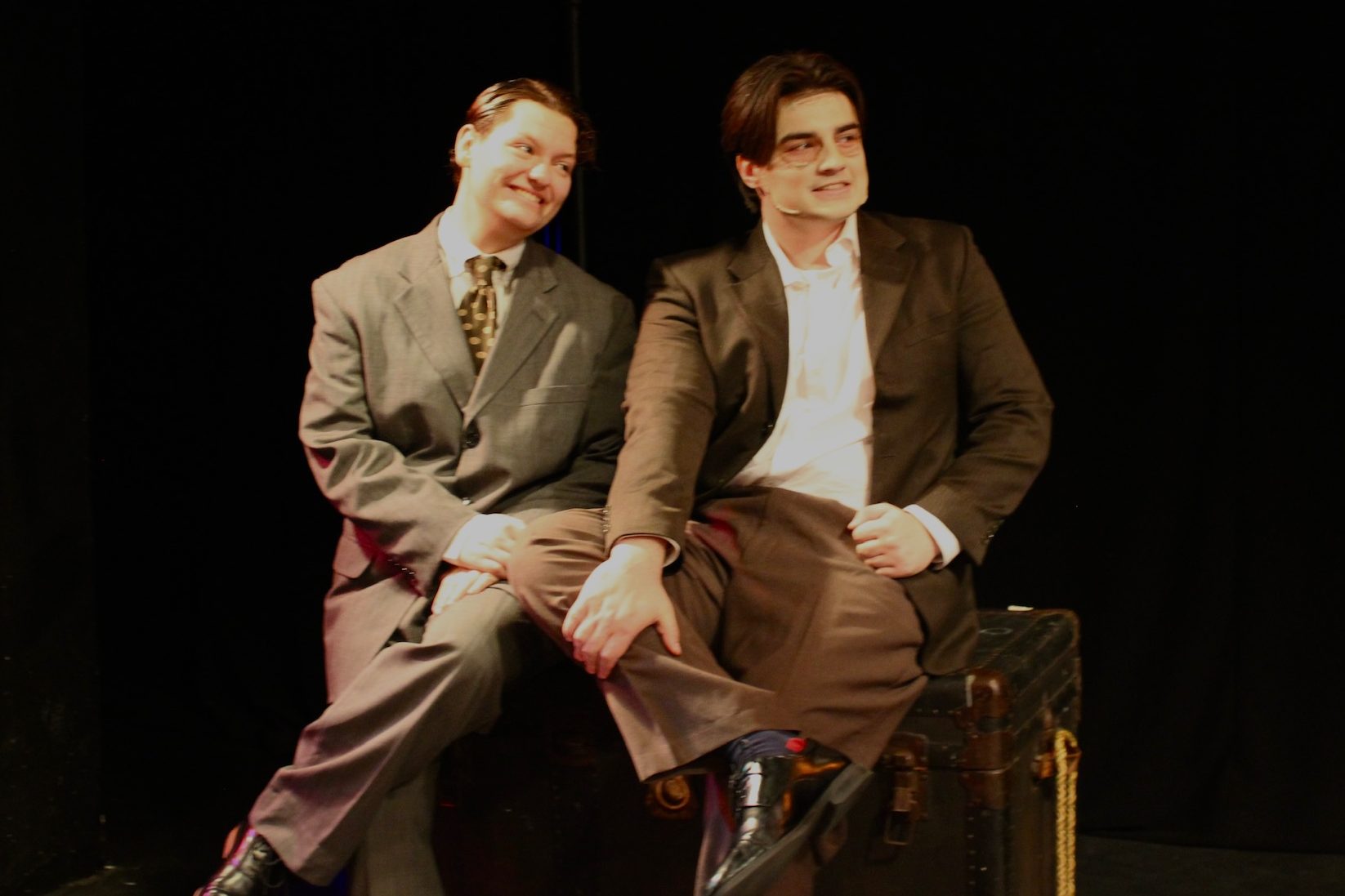 Tobias Sanders as Mortimer Brewster and Tyler Radze as Jonathan Brewster sitting on a trunk/window seat