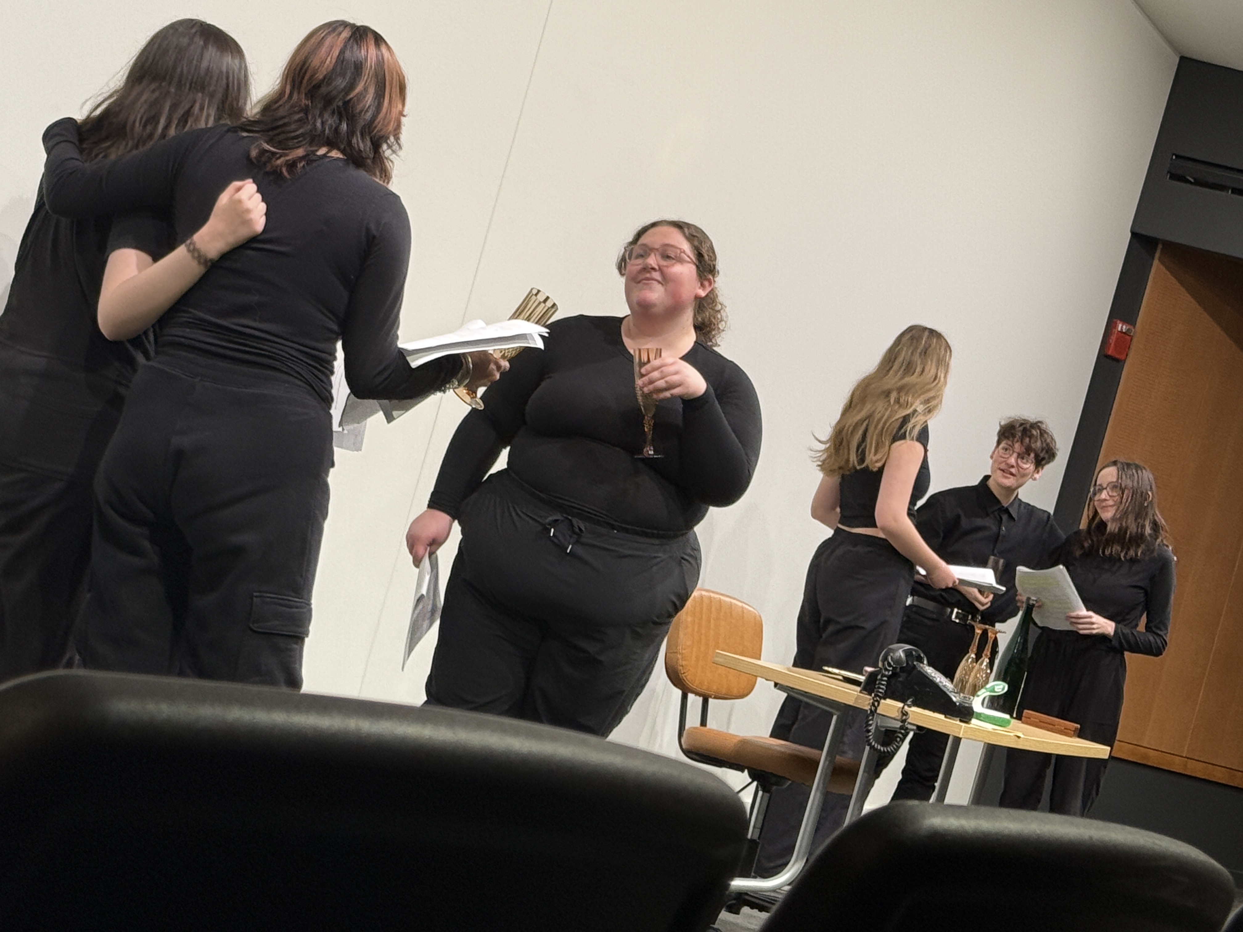 A cocktail party featuring Alison Mastee as Cady, Jhanvi Gugneja as Sebastian, Reese Verlinde as Margaret, Ella Galens as David, Tobias Sanders as Micheal, Caitlin Myers as Jo, and Veronica Thomas as Ezra in "Nuclear" at the Facility for Rare Isotope Beams (FRIB) produced by Second Stage Playwriting